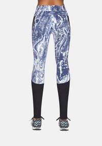 Legginsy sportowe z niebiesko-białym abstrakcyjnym wzorem, teksturowanymi czarnymi panelami na dolnych partiach nóg, zestawione z wzorzystymi sneakersami.