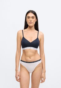 Granatowy biustonosz typu braletka z cienkimi ramiączkami i białą opaską z logo; do tego białe majtki z granatową opaską z logo. Gładki bawełniany materiał.