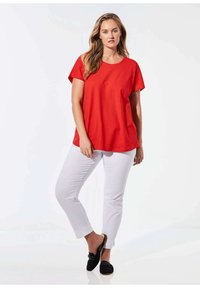 Rotes Baumwoll-T-Shirt mit lockerer Passform, kurzen Ärmeln und rundem Halsausschnitt, kombiniert mit schmalen weißen Hosen und schwarzen Slippern.