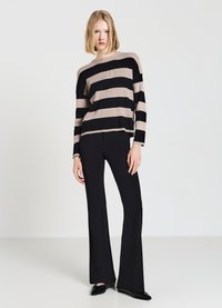 Striped knit sweater in beige and black, featuring wide horizontal stripes and a relaxed fit. Paired with fitted black flared pants.