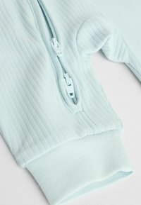 Lyseblå ribstrikket bodystocking med lynlåslukning og manchetter på ærmerne; har en glat tekstur og en diskret glans.