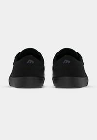 Μαύρα παπούτσια αθλητικά με λείο σουέτ πάνω μέρος και καουτσούκ σόλα, διαθέτοντας στρογγυλή μύτη και διακριτική λεπτομέρεια λογότυπου στη φτέρνα.