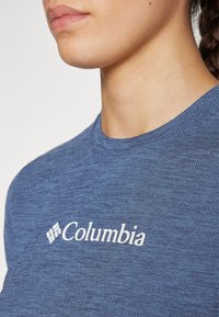 Sinine tekstuuriga lühikeste varrukatega särk, millel on ümberlõigatud kaelus ja ees valge "Columbia" logo. Pehme, hingav materjal.