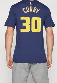 Camiseta de algodón azul marino con el número "30" en malla amarilla y el texto "CURRY" en la parte posterior. Con mangas cortas y diseño de cuello redondo.