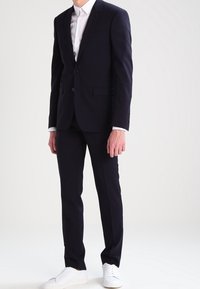 Marinblå kostym med smal passform, enfärgad jacka, notch-kragar och matchande byxor. Kombinera med vita sneakers för en modern touch.
