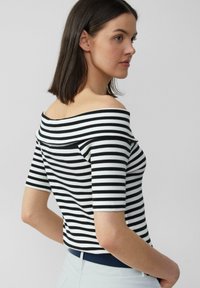 Top a righe bianche e nere, con scollo off-the-shoulder, maniche corte, design aderente, texture a coste e un'apertura del collo elegante.