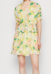 Blommönstrad klänning i gult, med korta puffärmar, v-ringning och dragsko i midjan med volangkant och livliga blommönster.
