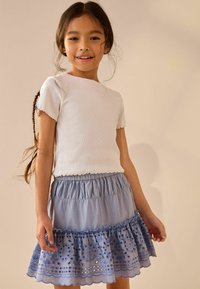 Haut blanc à manches courtes à rayures, associé à une jupe légère bleu clair à volants ornée de motifs brodés et dotée d'une taille froncée.