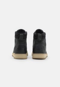 Botas de tobillo de cuero negro con un suave cuello de ante, suelas de goma beige y detalles cosidos; etiqueta con el logo en el talón.
