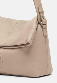 Beige Leder-Umhängetasche mit umgeschlagenem Deckel, verstellbarem Tragegurt, sichtbaren Nähten und dezentem Branding in der unteren Ecke.