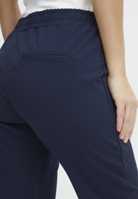 Mörkblå joggerbyxor med elastisk midja, slät textur och en enda bakficka. Tätt sittande design med avsmalnande ben.