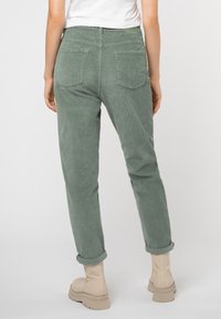 Grüne Cordhosen mit entspannter Passform und umgeschlagenen Säumen, ausgestattet mit Gesäßtaschen und strukturiertem Stoff, kombiniert mit beigen, klobigen Stiefeln mit Absatz.