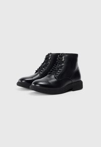 Botas de cuero negro hasta el tobillo con punta redonda, seis ojales de metal y suela de goma texturizada. Superficie lisa sin patrones ni acentos visibles.