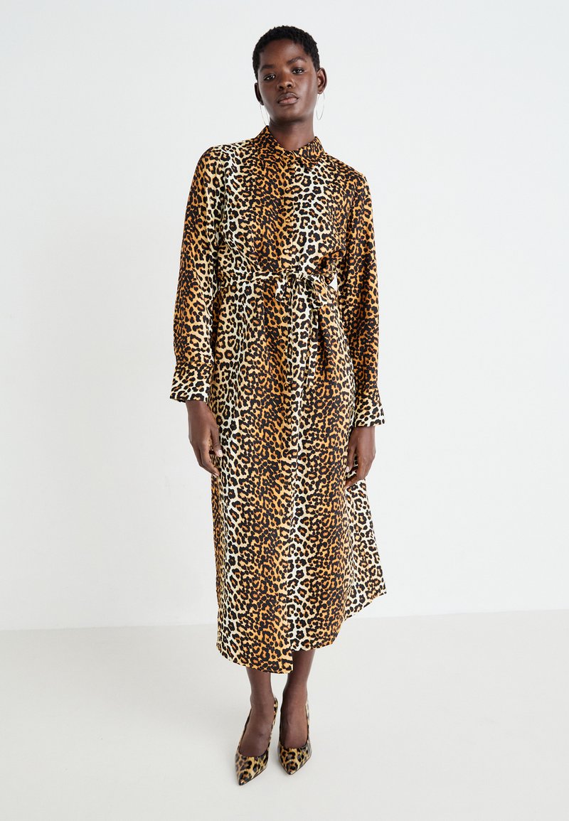 Abito con stampa leopardata che presenta maniche lunghe, colletto, vita con cintura e una silhouette fluida nei toni del marrone e del beige.