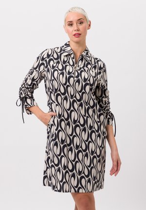 Ein knielanges Hemdkleid in Creme und Marineblau mit Wellenmuster, Frontreißverschluss und gerafften Ärmeln mit Bändern.