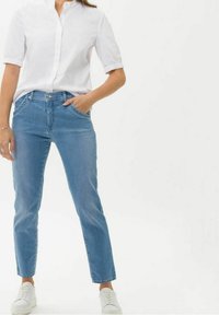 Ljust blå denimjeans med rak benmodell, i kombination med en vit skjorta med krage och vita sneakers. Enkelt och rent design.