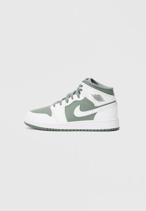 Baskets montantes Nike Air Jordan blanches et vert pâle avec lacets, logo de la marque sur le côté et semelle visible sur fond clair uni.