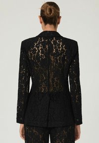 Must mustriga jakk, millel on lillemuster, pikad varrukad, terav krae ja üks selja avaus, et tagada õige sobivus.