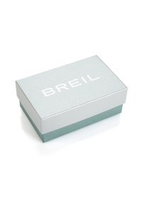 Caja de regalo rectangular con una superficie plateada brillante y base azul verdoso. Presenta un texto en negrita en blanco "BREIL" en la parte superior. Textura suave.
