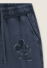 Pantalons de survêtement bleu marine foncé avec ceinture élastique, poches latérales, présentant un motif de Mickey Mouse en strass et un texte imprimé en dessous du graphique.