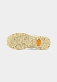 Semelle de chaussure beige avec un motif de bande de roulement angulaire et un logo Vibram orange près du talon sur un fond blanc.