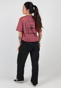 T-shirt bordeaux avec un design graphique noir au dos, assorti à un jean noir taille haute et des baskets noires. Texture lisse.