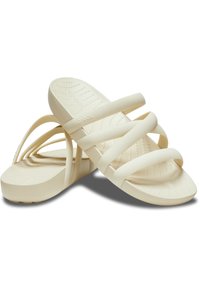 Sandali incrociati beige chiaro realizzati in gomma con un plantare sagomato e una texture puntinata sulla soletta, caratterizzati da un design a suola piatta.