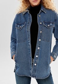 Lichtblauwe denimshirt met twee borstzakken, zilveren knopen en studaccenten op de kraag, met een relaxte pasvorm en lange mouwen.