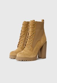 Tan faux suede enkellaarsjes met een chunky hak, voorzien van gouden oogjes, een vetersluiting aan de voorkant en een geribbelde sokachtige textielpaneel.