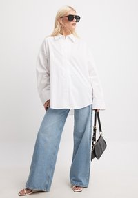 Baltas pārslēgts krekls ar pogām, gaismas zilas platas kājas džinsi, melna rokassoma un tumši saulesbrilles. Gluda auduma, taisna piegriezuma, ikdienišķs dizains.