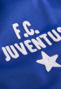 Blått tyg med broderad text "F.C. JUVENTUS" i vitt, ackompanjerad av en vit stjärna, som visar en slät textur och prydlig sömnad.