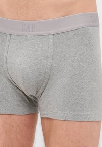 Boxer-briefs en coton gris avec une ceinture élastique douce comportant le texte "GAP" en relief. Texture lisse et design ajusté.