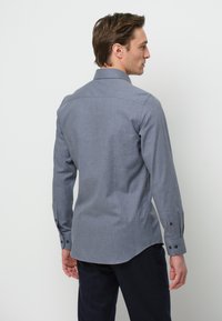 Camicia grigia a maniche lunghe con colletto button-down, dettaglio sulla parte posteriore e polsini con bottoni. Tessuto liscio con una leggera texture.