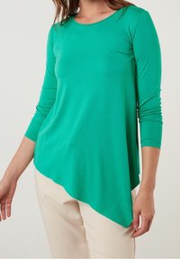 Grön långärmad topp med rund halsringning och asymmetrisk kant. Mjuk, lätt material med en slät yta.