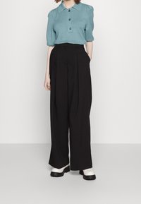 Světle modrý pletený polo s krátkými rukávy a třemi knoflíky, v kombinaci s vysokými černými kalhotami s širokými nohavicemi a bílými platformovými botami.