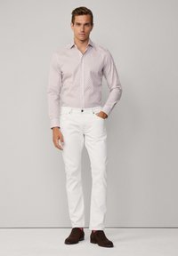 Witte denim broek gecombineerd met een rood-wit gemusterd overhemd met lange mouwen. Bruine suedepumps met roze accenten maken de outfit compleet.