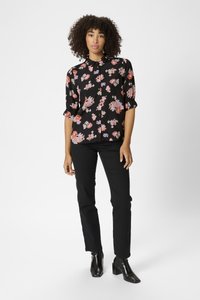Blouse noire à fleurs avec des manches courtes, ornée de motifs de fleurs multicolores. Associée à des pantalons slim noirs et des bottines à talons noires.