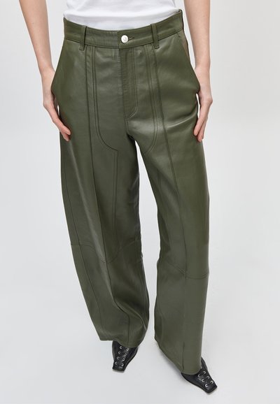 Χακί δερμάτινο παντελόνι ψηλής μέσης με ραμμένες πινελιές, φορεμένο με μαύρα δερμάτινα παπούτσια με τετράγωνη μύτη και κορδόνια και λευκό τοπ.