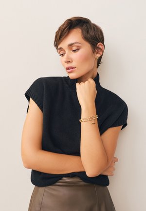Black knit sweater with short sleeves, paired with a brown leather skirt. Notable gold chain bracelet on wrist, smooth texture.