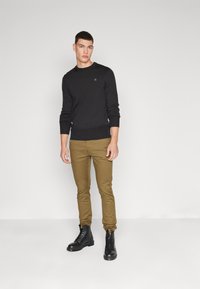 Schwarzer Pullover mit Rundhalsausschnitt, gerippten Bündchen und Saum. Olivgrüne Hose und schwarze Schnürstiefel. Einfaches Design, figurbetonte Silhouette.