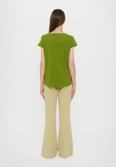Green short-sleeve top with a round neckline and contrasting stitching. Paired with beige flared trousers, showcasing a streamlined silhouette.