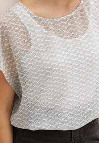 Blusa bianca con un motivo a onde ripetitive in nero. Tessuto morbido e leggero con scollatura rotonda e vestibilità ampia, orlo laterale curvo.