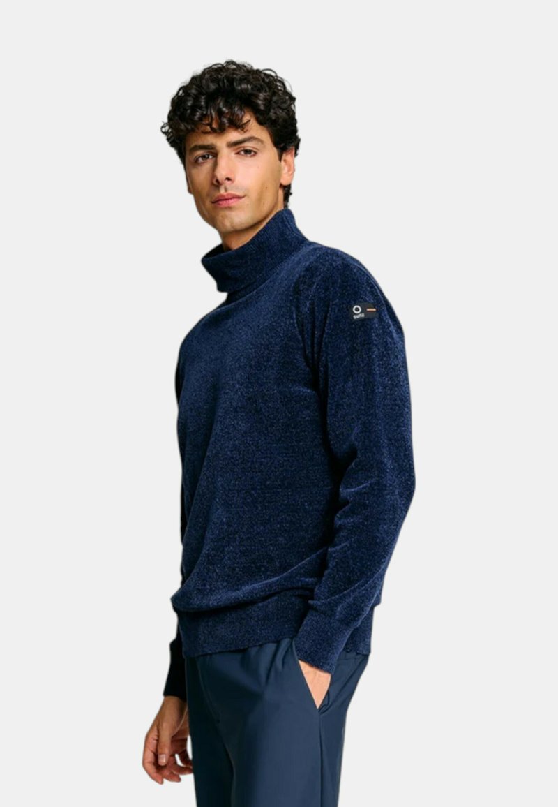 Maglione a collo alto blu navy in un tessuto morbido e testurizzato. Presenta una vestibilità rilassata e un accento con il marchio sulla manica sinistra.