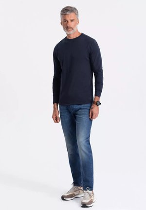 Marineblauwe lange mouw shirt, blauwe spijkerbroek en beige sneakers. Casual fit, gladde stof, ronde halslijn en subtiele stikseldetails.