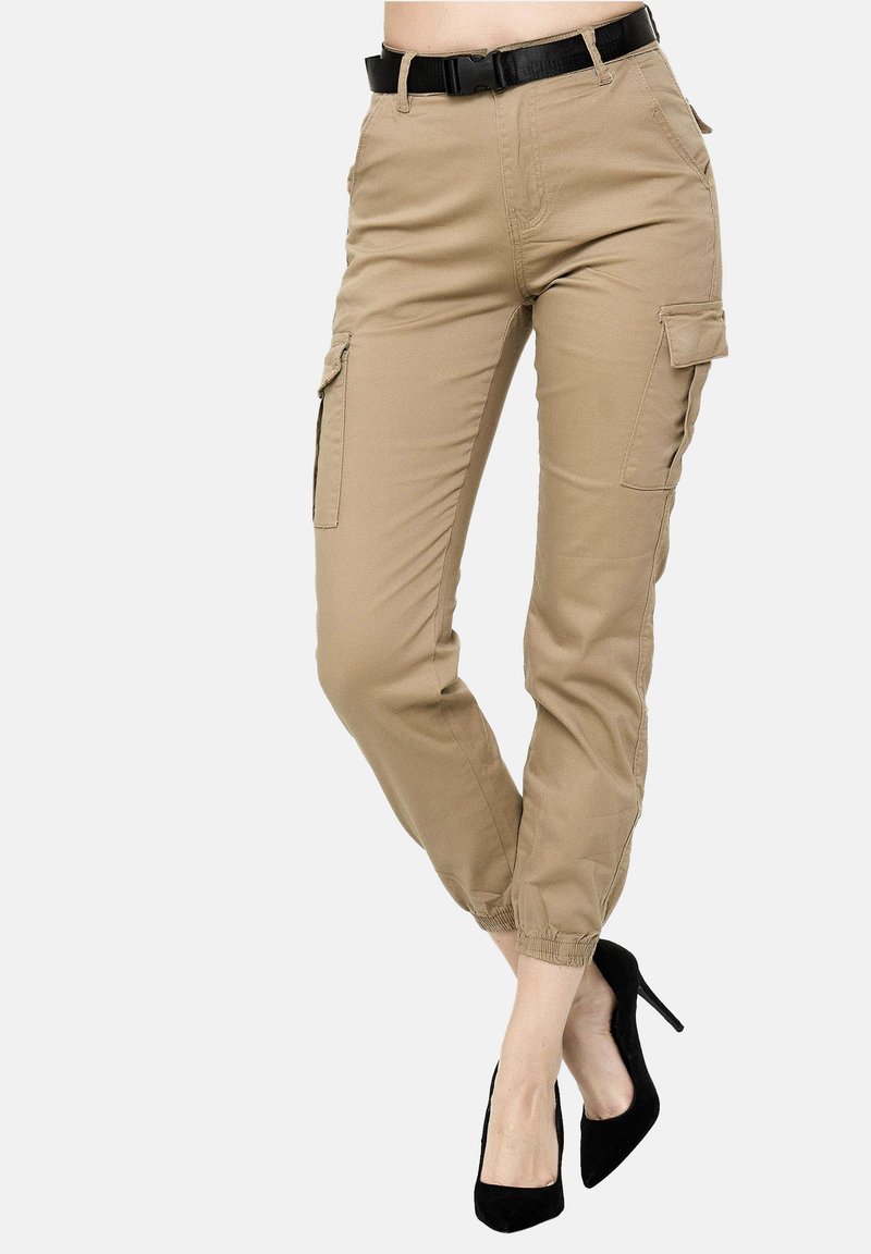 Beige cargobyxor med elastiska muddar, sidofickor och ett svart bälte. Materialet är slätt med en matt yta. Bärs med svarta klackskor.
