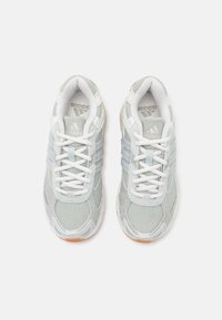 Vaaleanharmaat urheilukengät, joissa on valkoiset nauhat, kolme sinistä raitaa, tekstuuripinnat ja kumipohjat, joissa on hienovaraisia yksityiskohtia.