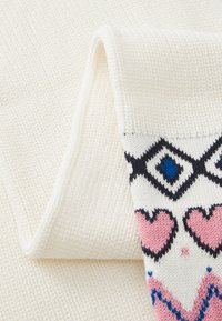 Tissu en coton tricoté blanc avec une section à motifs comportant des cœurs roses et des accents bleus sur un fond crème, plié à un angle.
