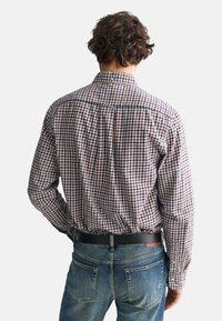Camisa de cuadros en marrón, azul y blanco; tejido de algodón; cuello estándar; costuras visibles; combinada con vaqueros azules y un cinturón negro.