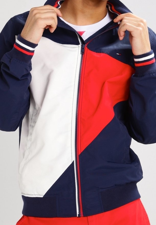 Marinblå och röd vindjacka med vita detaljer, med dragkedja fram, ribbade muddar och nederkant, samt geometrisk färgblockeringsdesign.