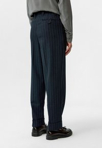 Donkerblauwe broek met streepdessin en een relaxte pasvorm, voorzien van een omslag aan de zoom en een achterzak met knoopdetail.
